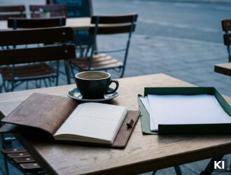 Schreibtisch im Morgenlicht mit Notizbuch, drei handgeschriebenen Fragen und einem Ordner mit unvollständigen Kostenangaben: Hilfsmittel für den richt